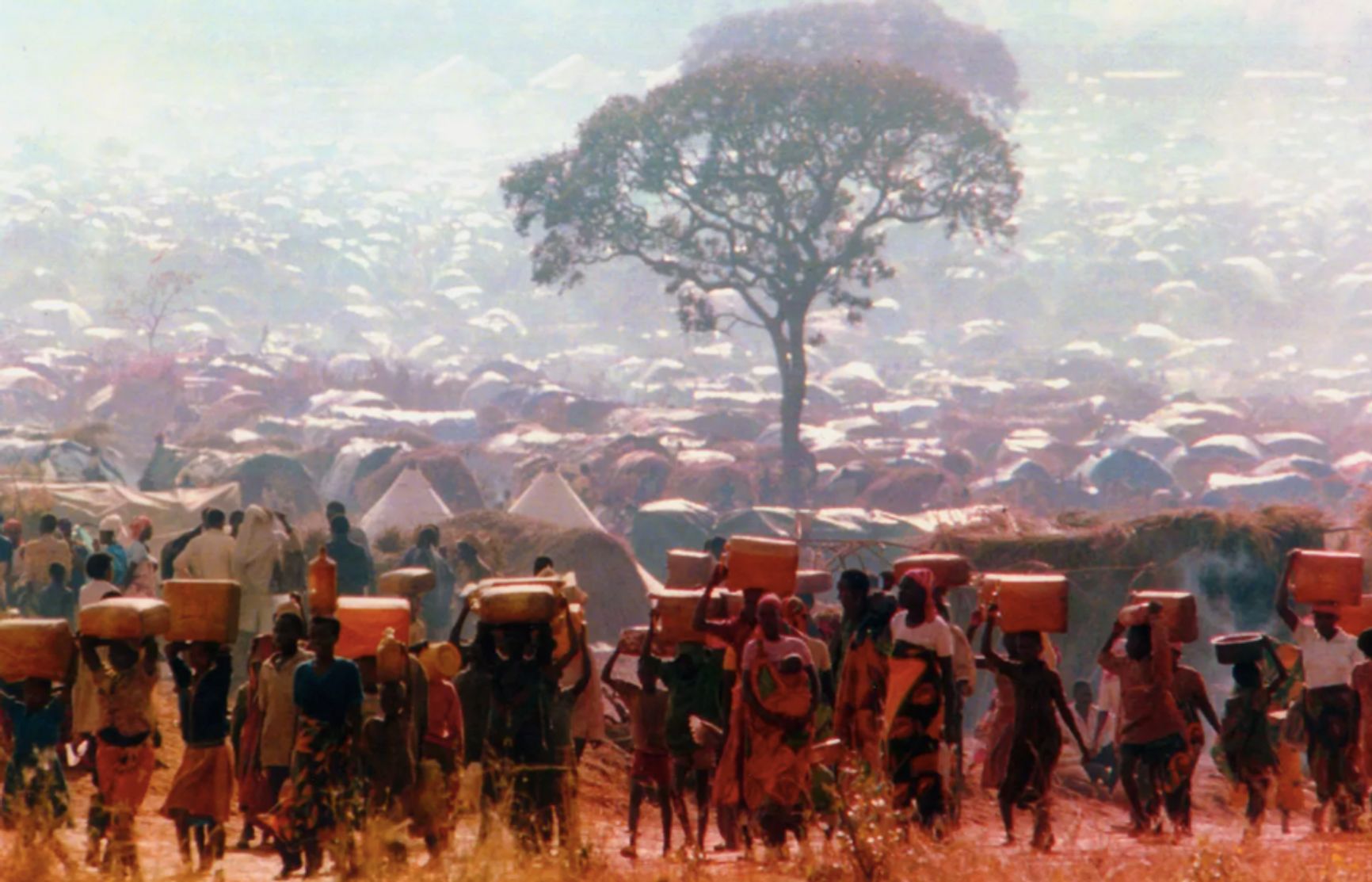 Спасшиеся от этнической чистки руандцы несут контейнеры с водой к своим хижинам в лагере беженцев Бенако в Танзании 