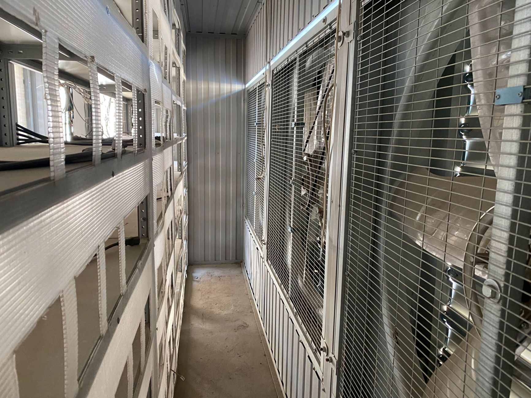 The inside of a shipping container converted into a crypto mining room, with shelves for ASIC miners on the left and fans on the right