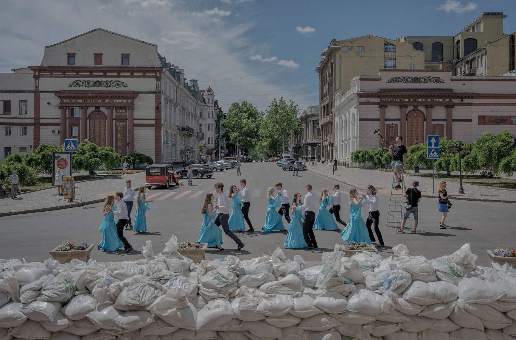 Выпускники школы танцуют у мешков с песком, защищающих фасад оперного театра в Одессе, 15 июня
