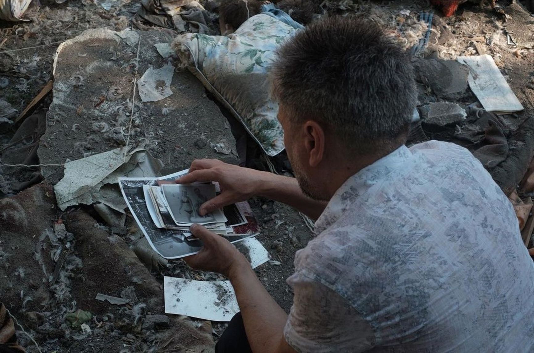 A man collects photographs of his relatives scattered near the destroyed five-story building, Mykolaiv  