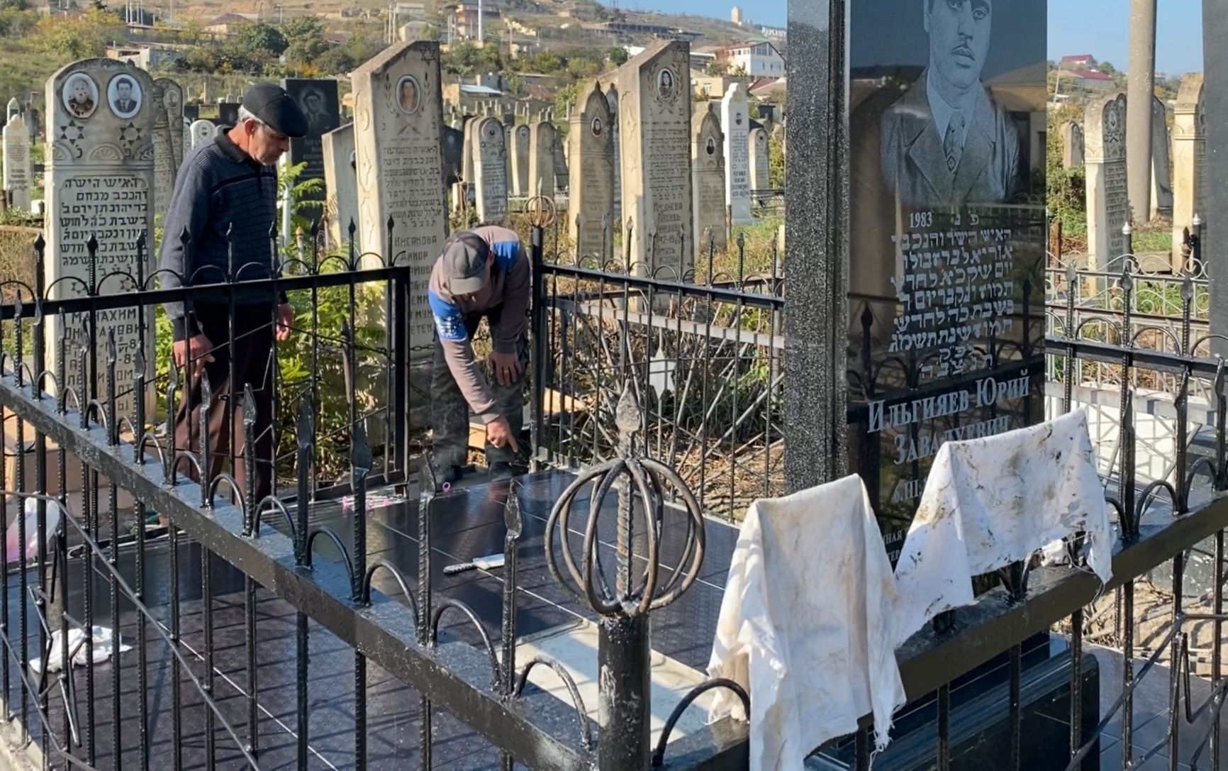 A cemetery visitor and a worker lay tiles at a Jewish cemetery in Derbent