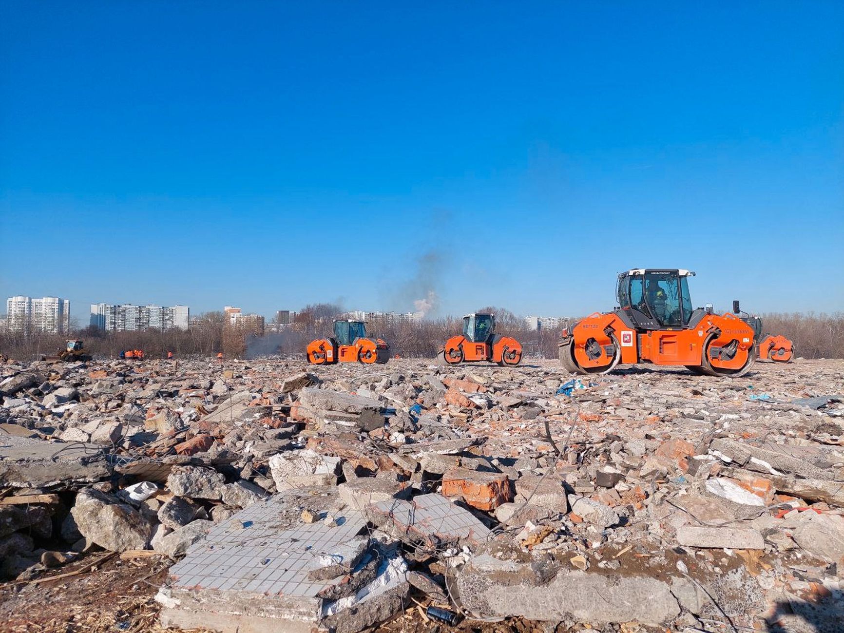 The construction machinery levels the terrain, filling in a layer of construction debris, including large debris from houses demolished under the renovation program