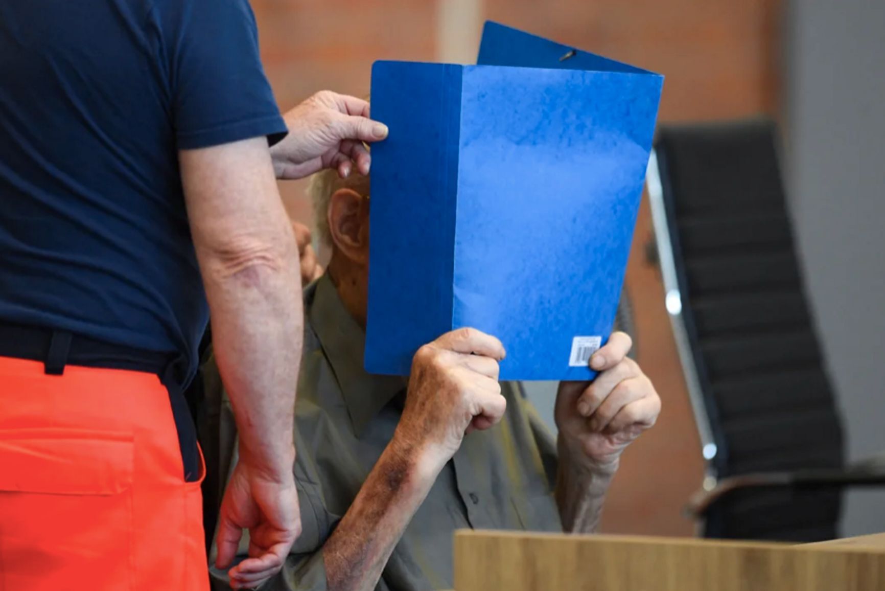 Josef Schutz obscures his face with a folder in all photographs from the court