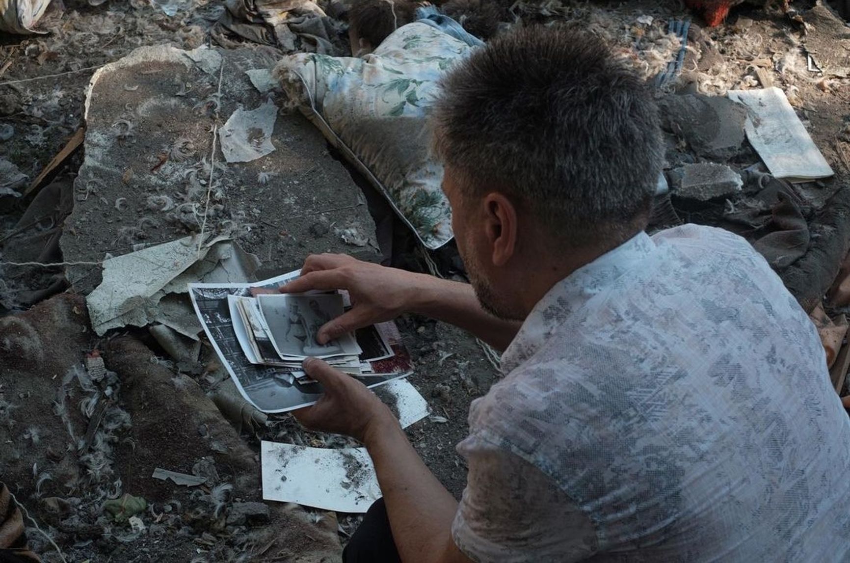 Мужчина собирает фотографии своих родных, разбросанные возле разрушенной пятиэтажки, Николаев